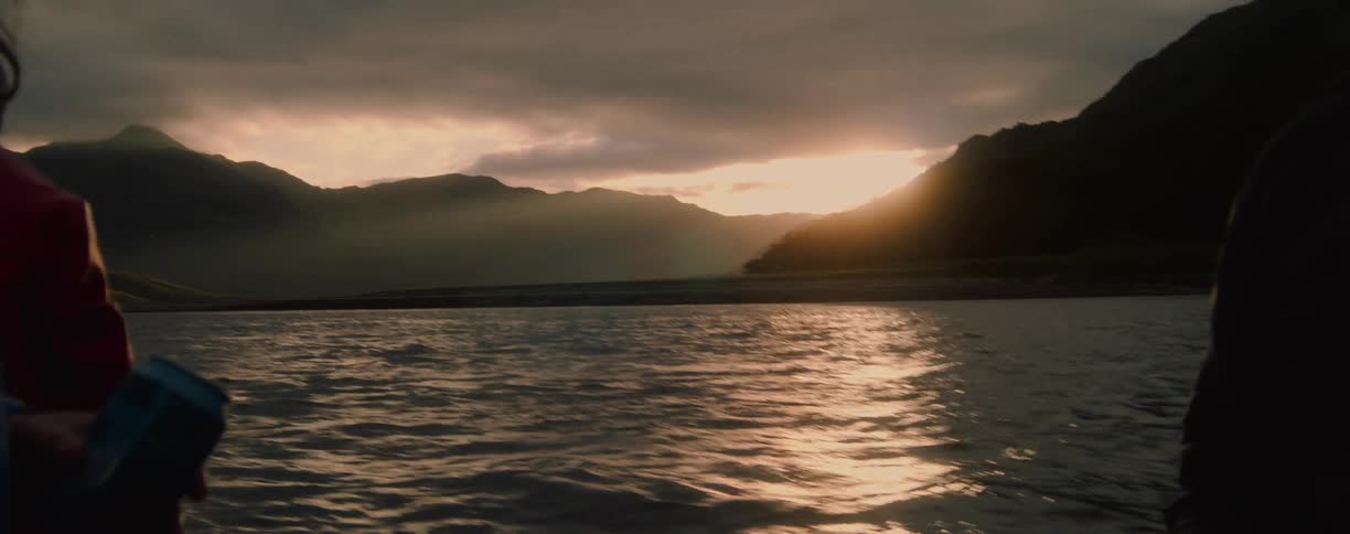 A group of people on a boat in a lake watching the water flow rapidly at sunset with a mountain range in the backdrop