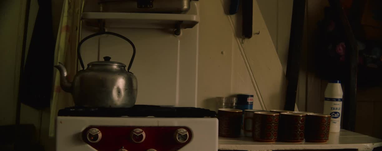 Aluminum kettle on an old stove beside mugs and seasonings