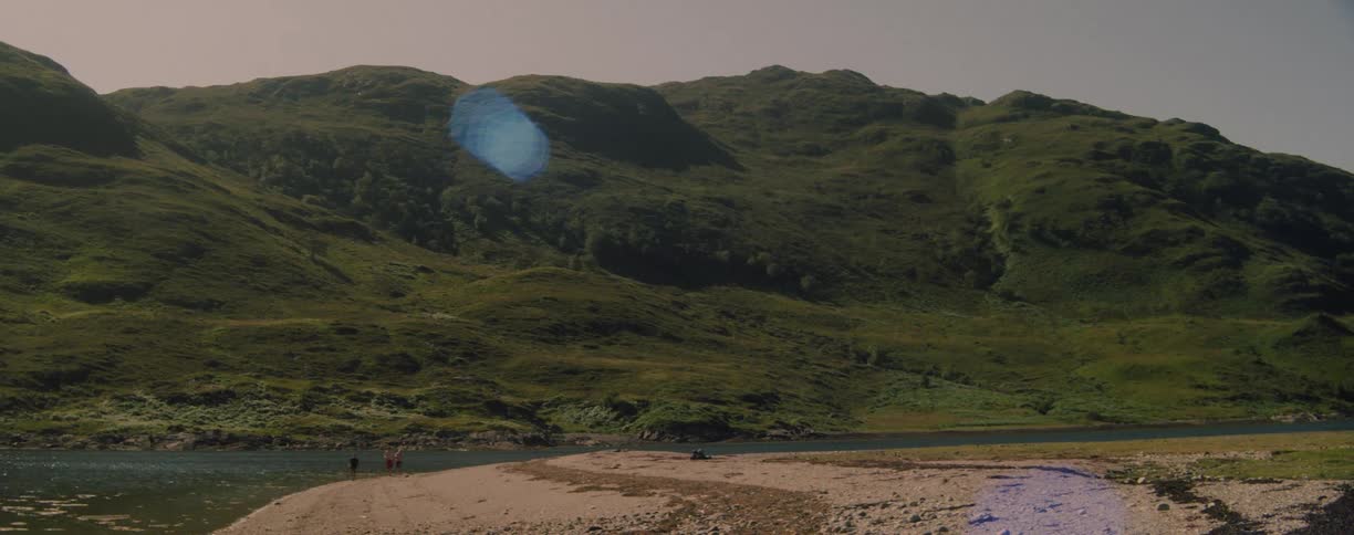 Green mountains surround a river with a strip of sand in the foreground