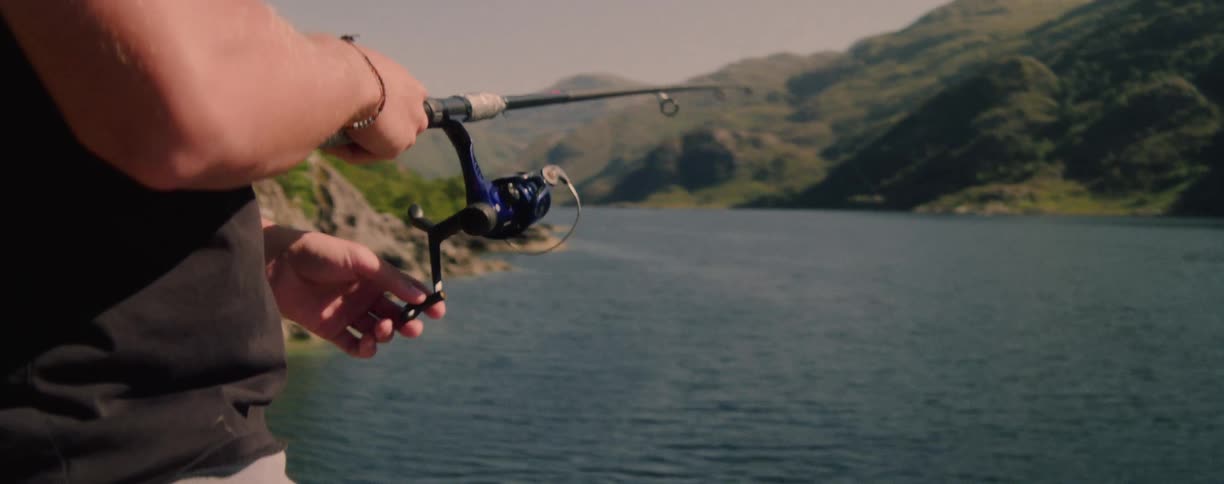 Man fishing in the mountain river valley turns the reel on his fishing rod