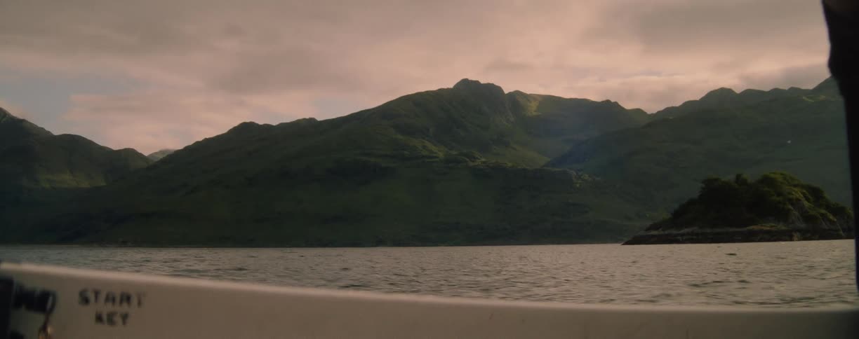 View of green mountains and rocky island from a boat on the lake