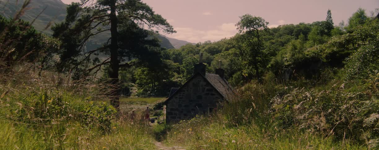 A small group of people exit a small house located in a remote mountain area