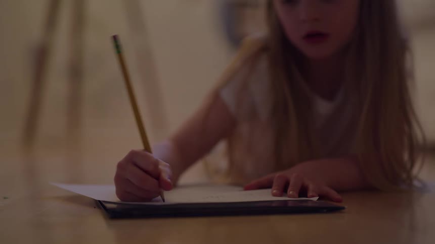 A girl uses a pencil to write while laying on the floor