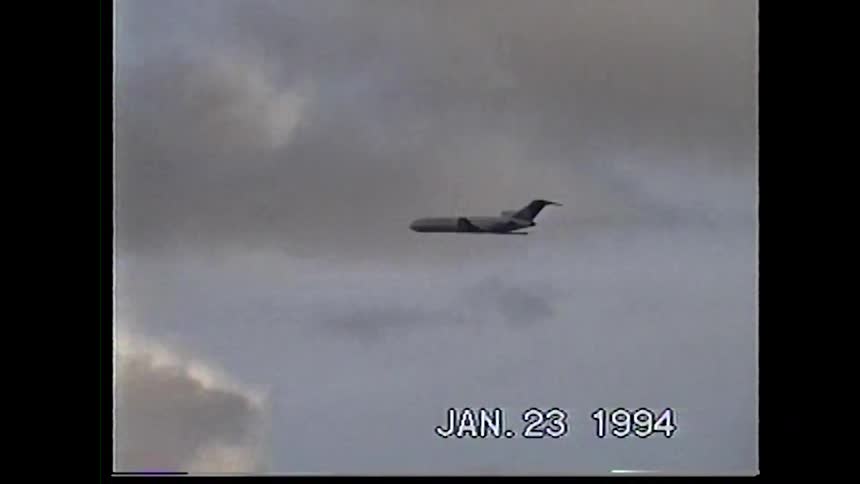 A commercial airplane flies across a cloudy sky