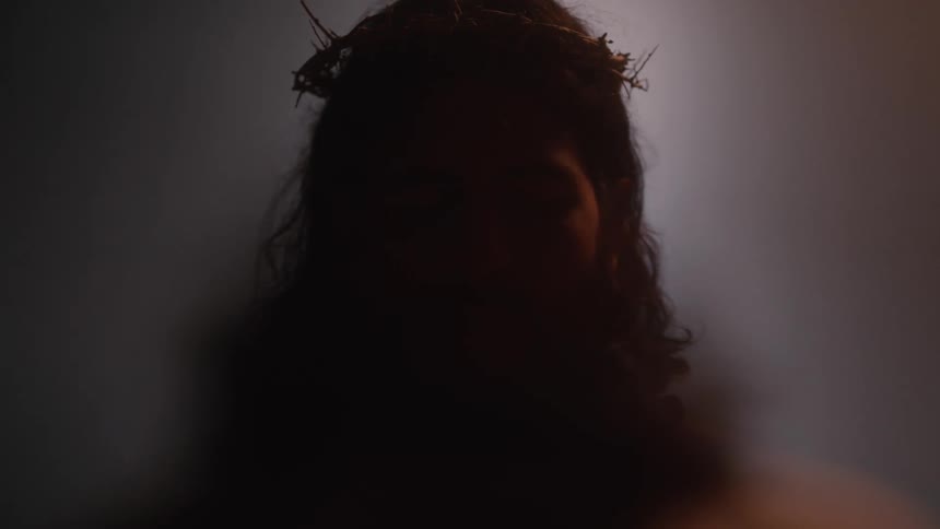 A young woman in a dimly lit room wearing a crown mask made of dry grasses on her head