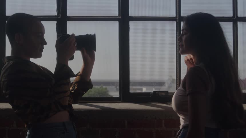Person photographs a woman near a window lit by natural light