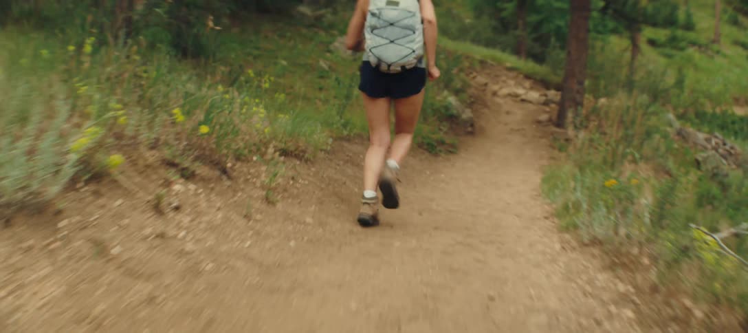A young girl running on a trail path in the woods carrying a backpack at midday