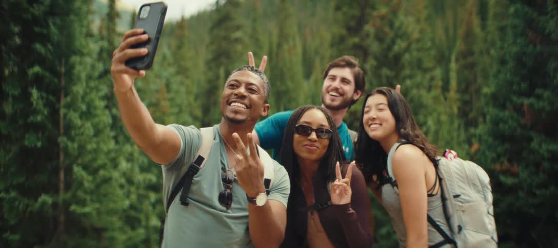 A group of four friends joyfully taking a selfie with a smartphone in a green mountain setting
