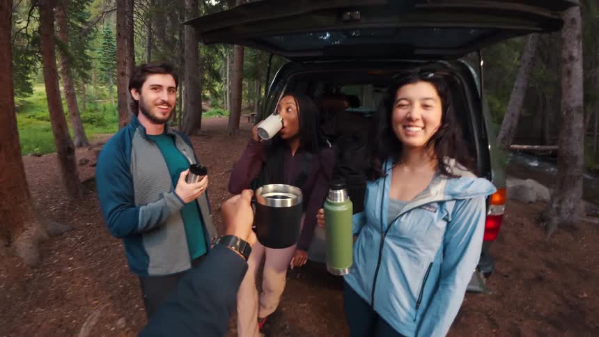 A group of friends sharing drinks in forest during a camping trip