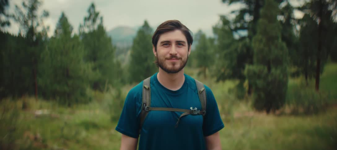 A lone hiker smiling and looking at the camera in a forest