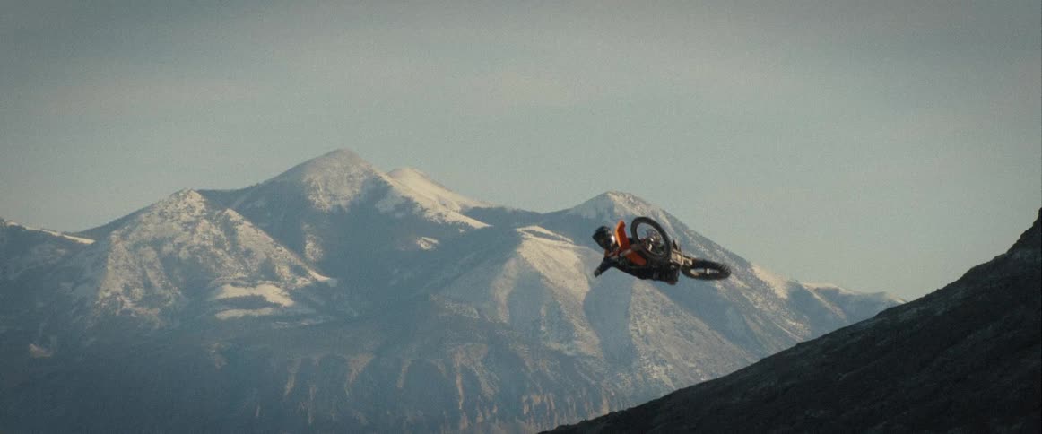 Motorcyclist performs an aerial stunt in front of snowy mountains
