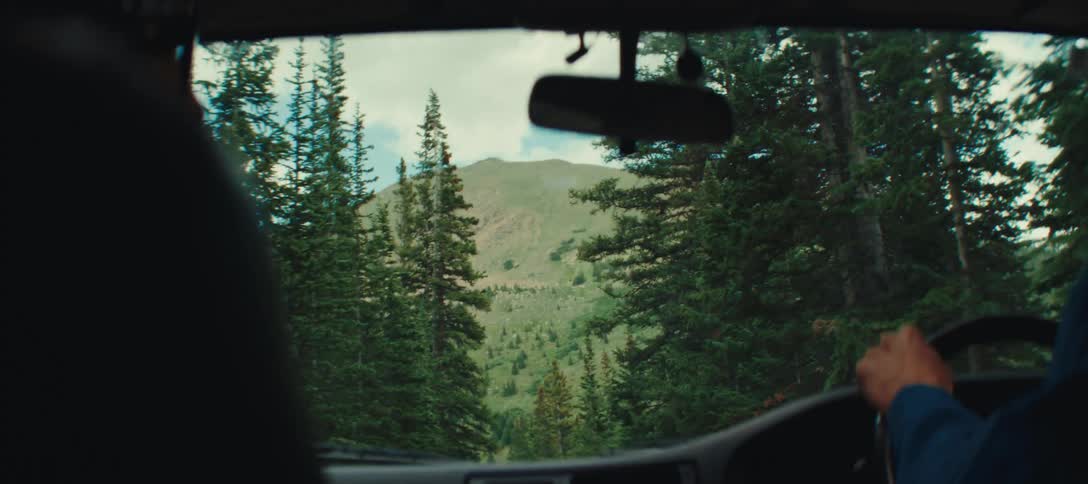 A car driving down a forest road in the direction of a mountain