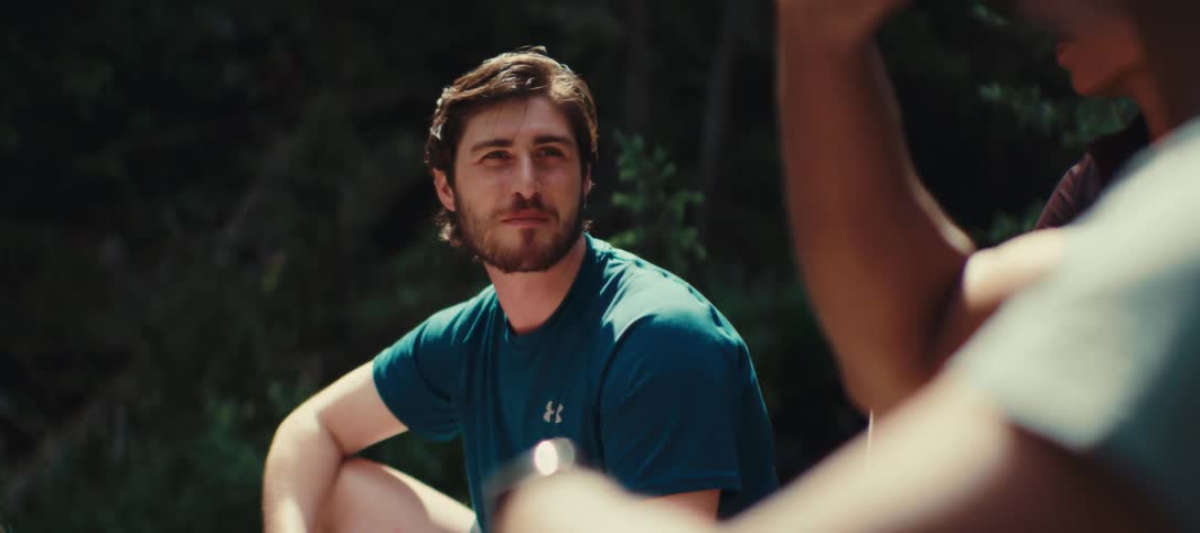 Man in a blue tshirt smiles while talking outdoors