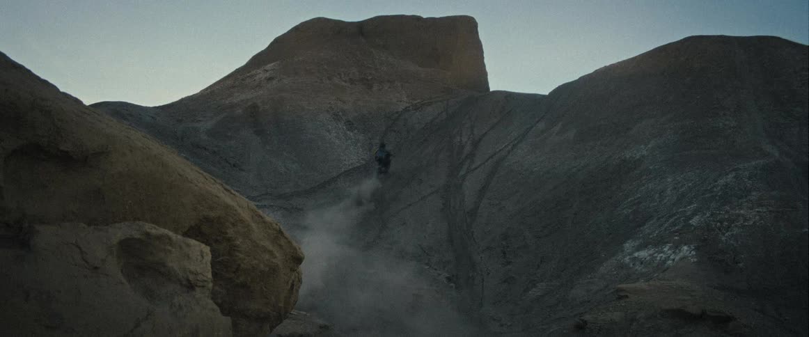 A man on a dirt bike is descending a steep dusty mountain slope the bike kicks up a cloud of dust and rocks as he rides down the rugged terrain