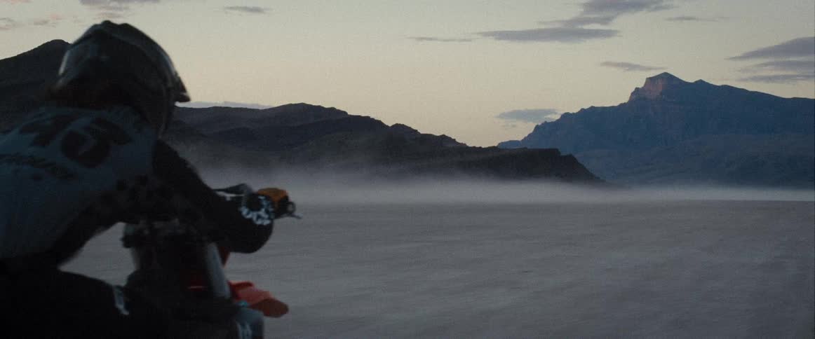 A lone person on a dirt bike in a foggy open expanse surrounded by mountains