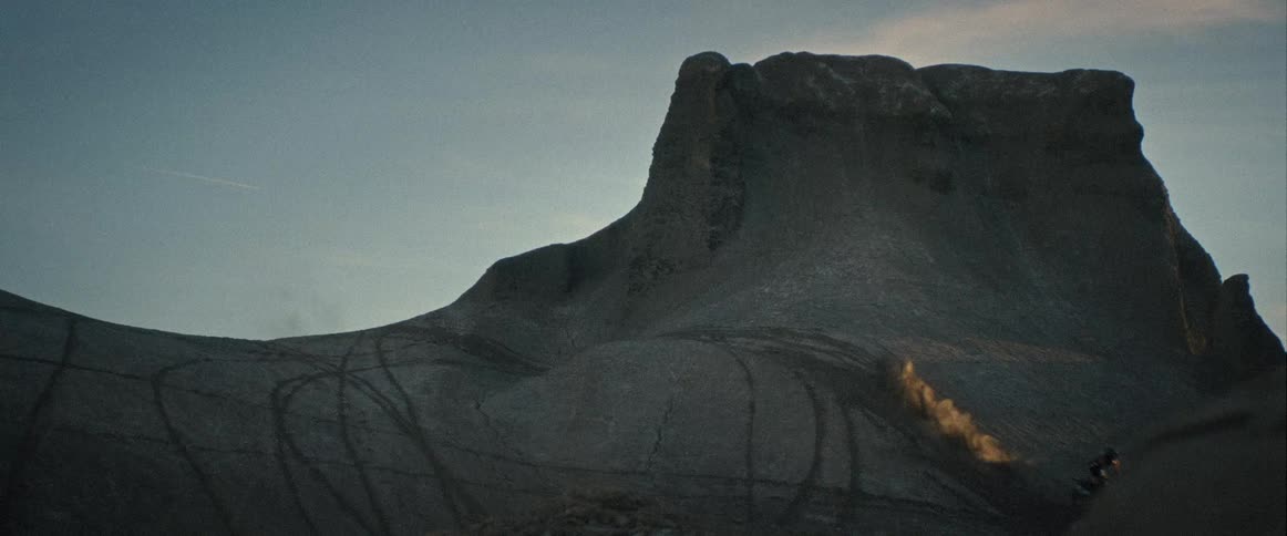 A mountain biker riding down a rock in the wild at sunset