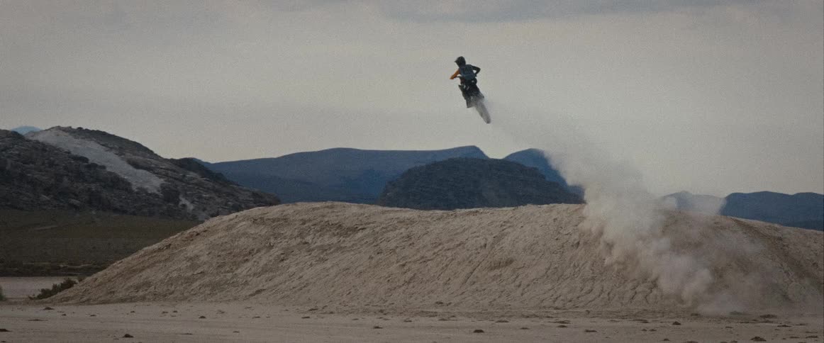 A motocross rider performing a mid air stunt against snowy mountains