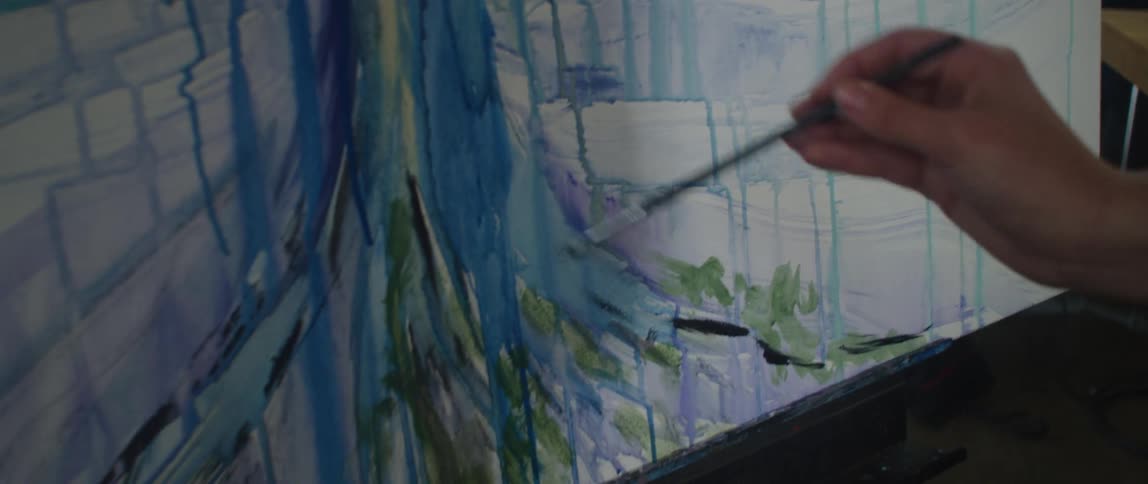 The video shows an artists hand using a paintbrush to add strokes of dark green paint onto a large canvas the canvas is covered in a mix of blue green and white brushstrokes that form an abstract painting