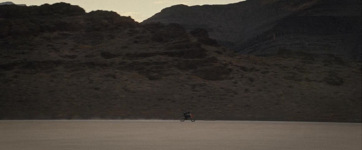 A lone individual drives their motorcycle across an expansive dried lake bed