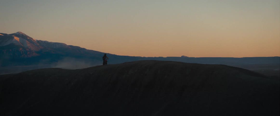A lone biker rides a ridge at sunset with mountains behind