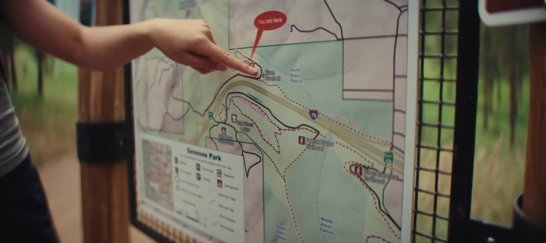 Person points to a map of genesee park on a trail board