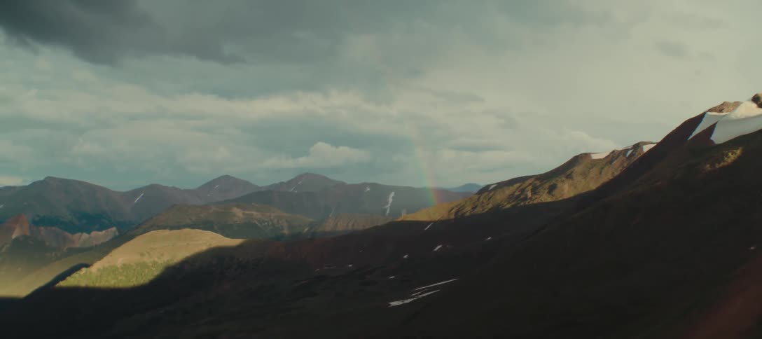 Sunlit mountains with a rainbow under a cloudy sky