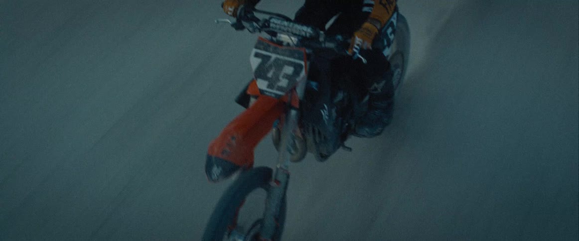 The video shows a lowangle shot of a person on a dirt bike wearing a helmet and full gear they ride across a flat open area kicking up a trail of dust as they speed past the camera