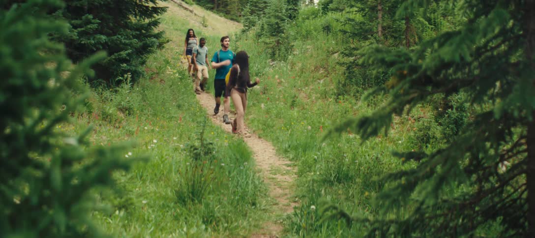 A group of friends hike together along a narrow forest trail