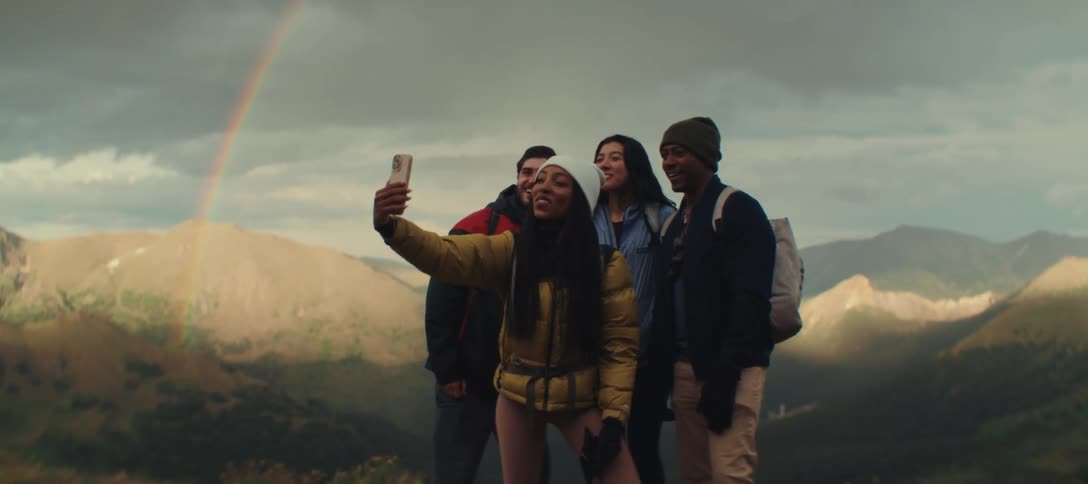 Group of friends takes a selfie in front of a rainbow in the mountains
