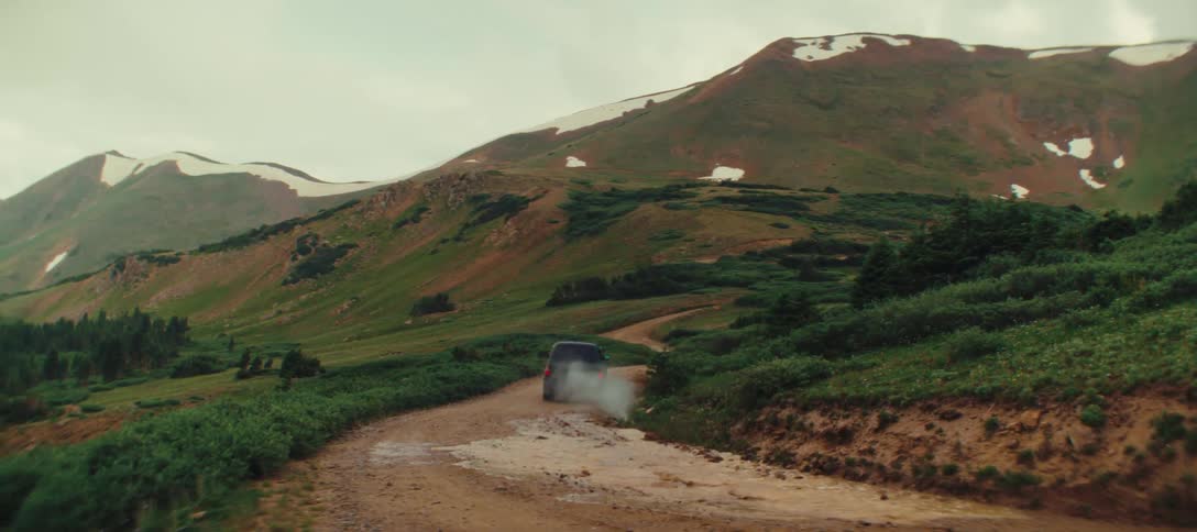 A black suv drives through a muddy mountain road