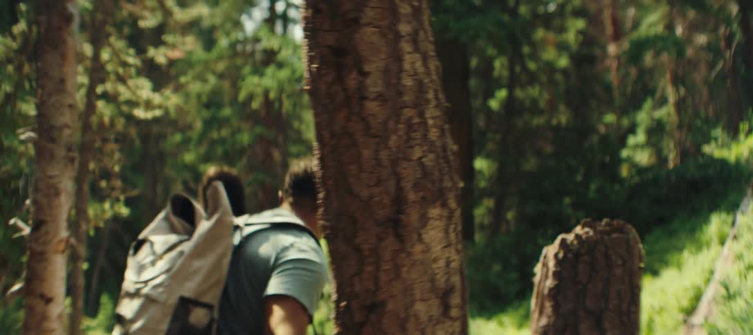 A group of friends with backpacks hike through a dense forest walking alongside a small stream