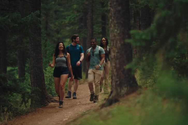 A group of friends smile and talk while they walk along a forest trail