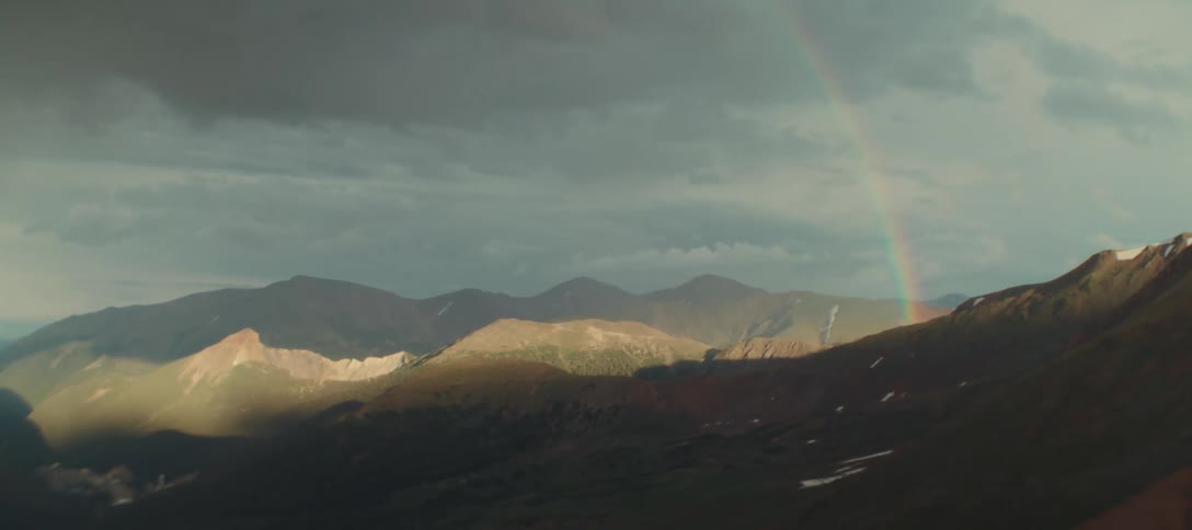 A rainbow arcs over sunlit mountains after a storm