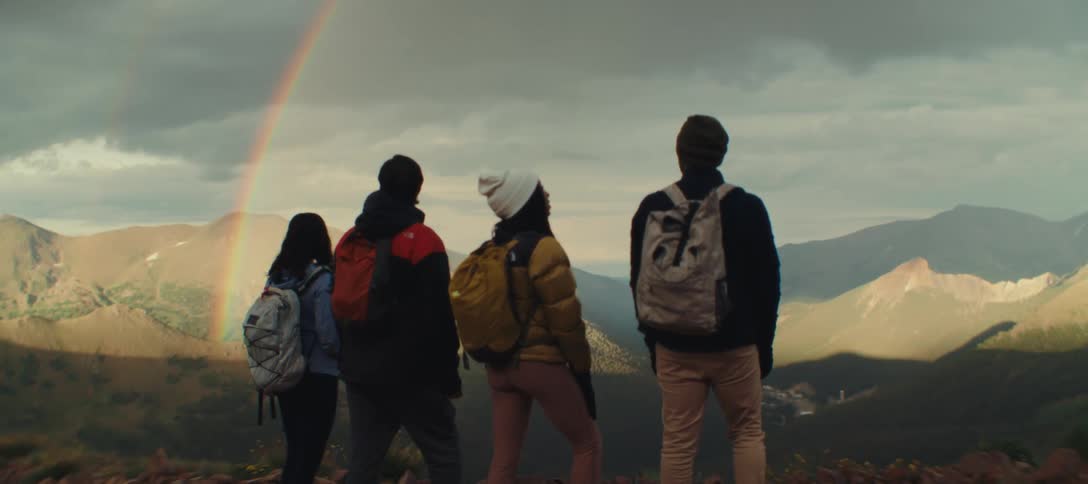 Four hikers admire a rainbow stretching over a mountain valley