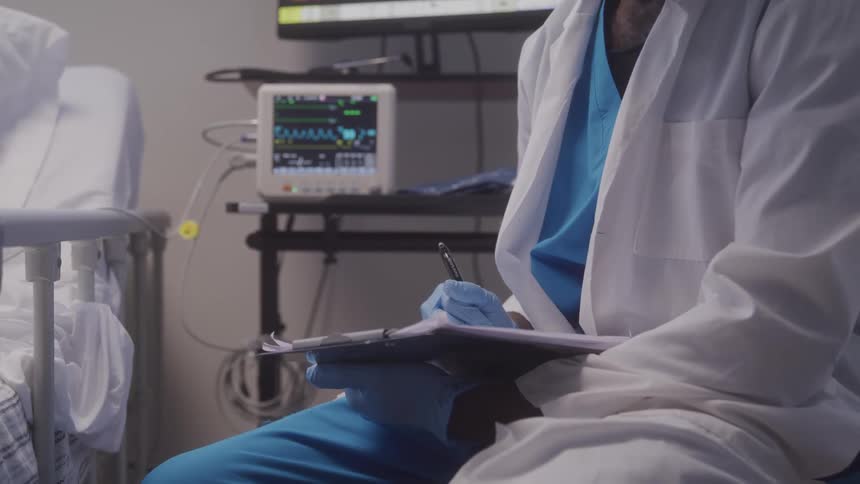 Healthcare professional taking notes beside a patient in a hospital bed