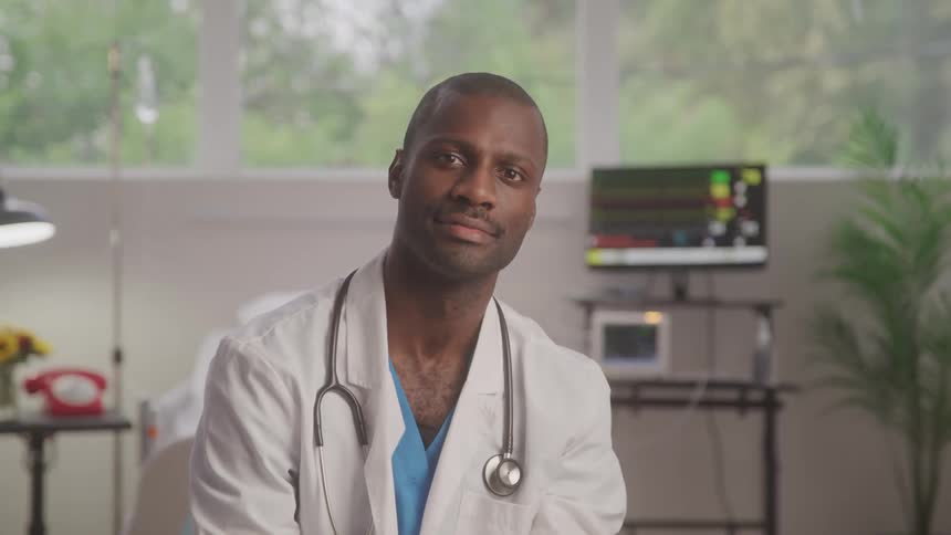 Male doctor sits in medical office looking into camera
