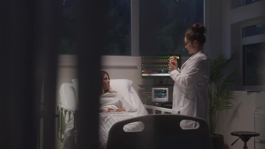 Doctor talks with patient lying in a hospital bed next to monitoring equipment