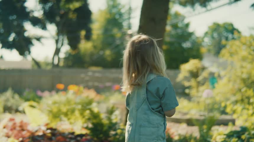 Blonde girl walks through a large garden in the backyard on a sunny day