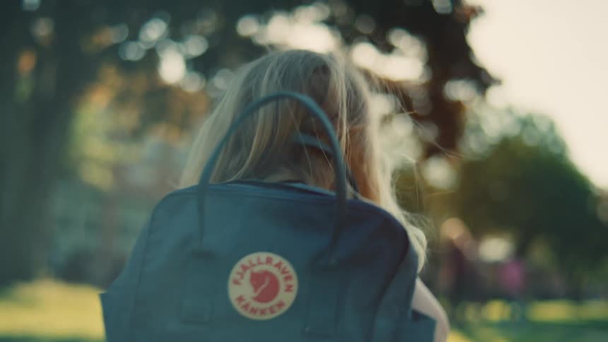 A young girl with a blue backpack walking towards a school building on a sunny day