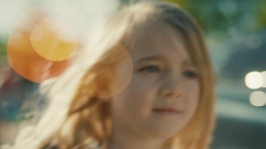 Blonde elementary school aged girl walks along the street on a sunny day while carrying a backpack