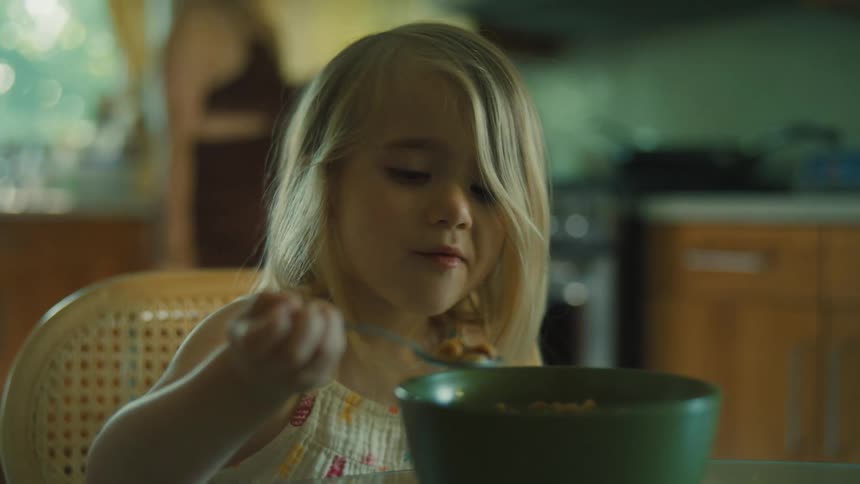 The first video shows a young girl eating cereal from a bowl at a table the second video shows a person kitesurfing across the water using a large kite to pull them on a board