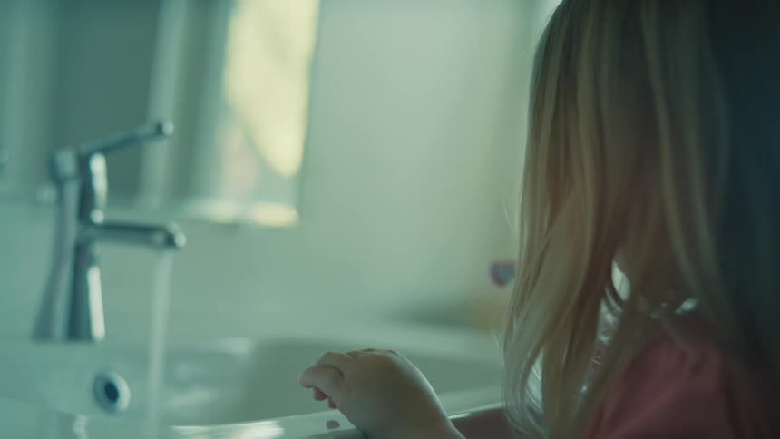 A young girl brushes her teeth in front of a bathroom mirror