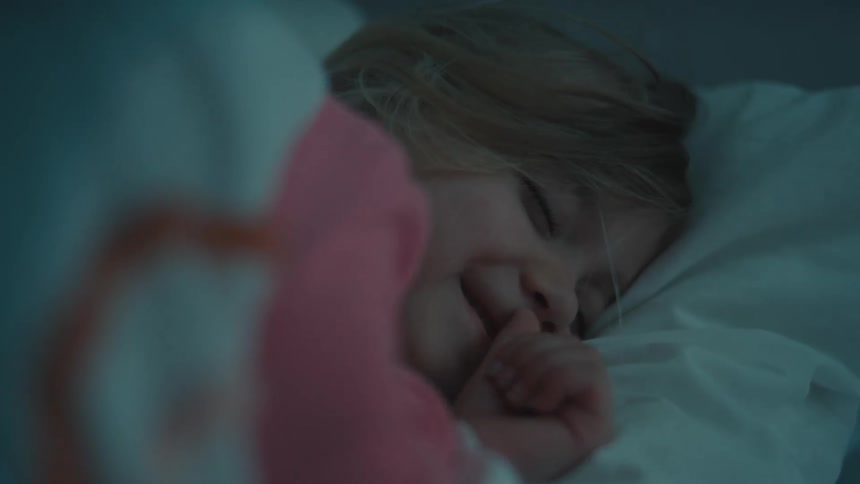A child lies on a bed covered with a blanket laughing and looking excited