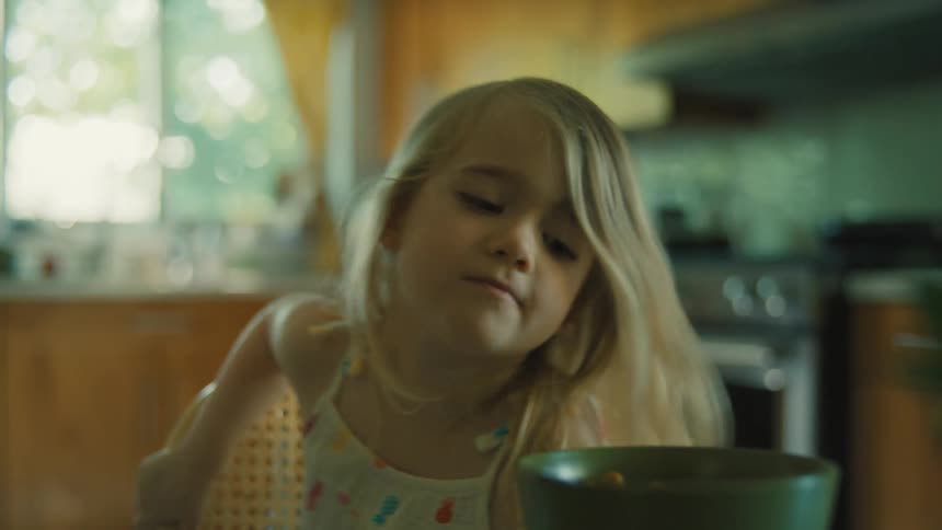 A young child sits at the table as their mother serves breakfast