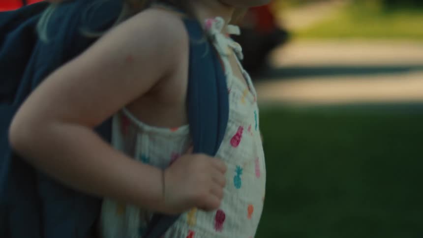 A young girl walks outdoors with a backpack