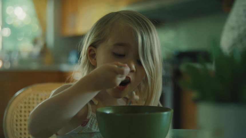 Blonde child has breakfast eating from a green bowl at the table