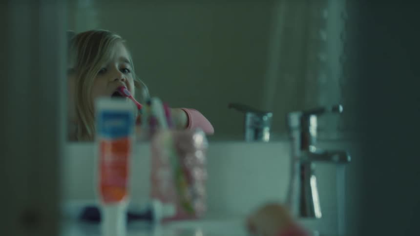 A child is brushing their teeth in front of the bathroom mirror