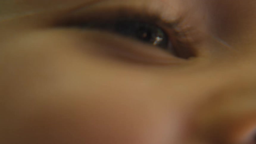 The video shows a macro shot of a persons eye which is dark brown the camera is out of focus at first but then sharpens to reveal the details of the eyelashes and iris