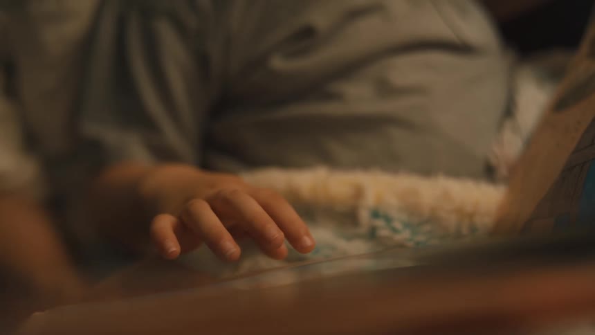 A little girl with lightcolored hair is holding and looking at a book her hand is on the pages and she appears to be reading or looking at the pictures