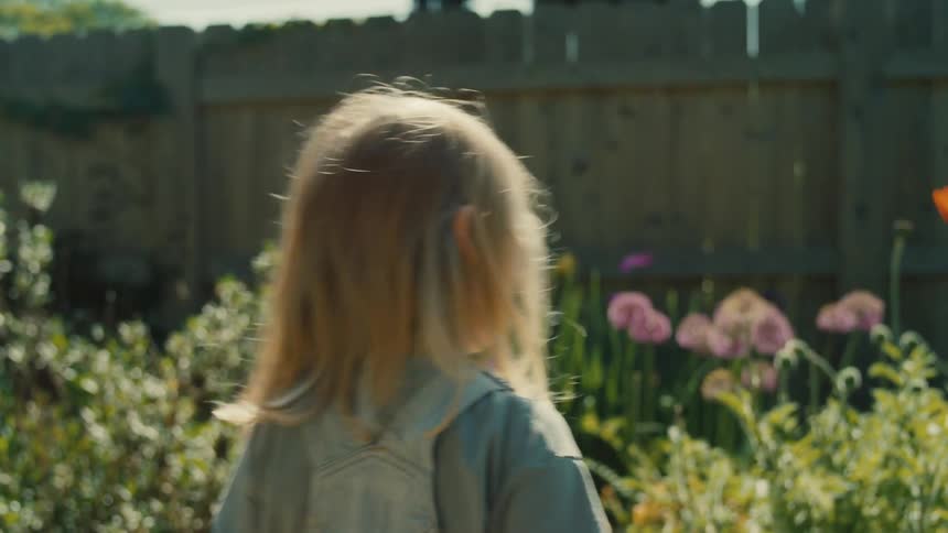 Girl walking around the flower garden in the backyard points at different flowers and plants